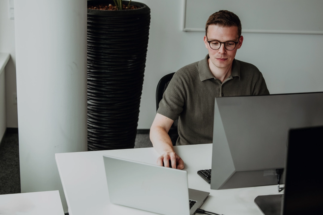An experienced employee works focused at a laptop and monitor in a modern office—independent work, professional expertise, and strong development opportunities for experienced professionals at BSI Software.