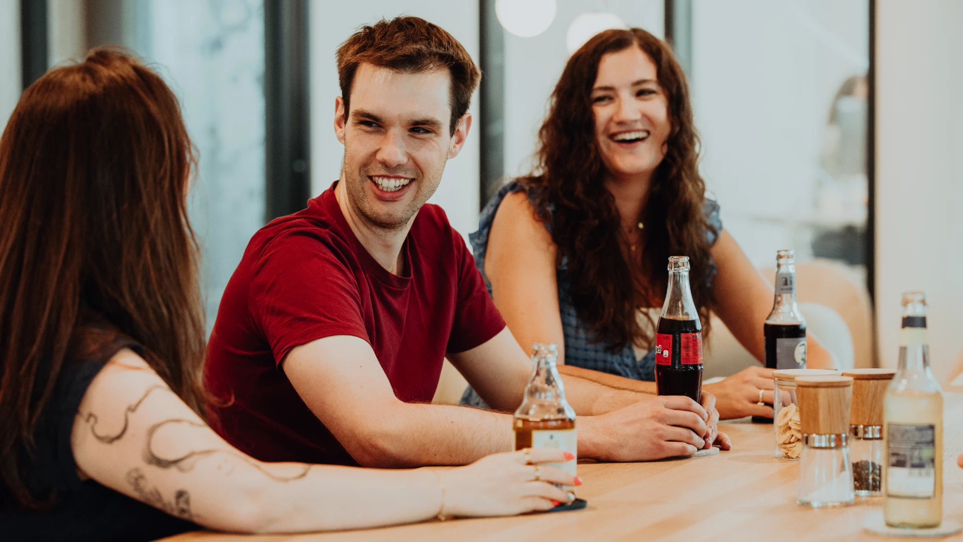 Three employees sit together, laughing and chatting over drinks—an open, friendly atmosphere and strong team culture at BSI Software that makes everyday work engaging and human.