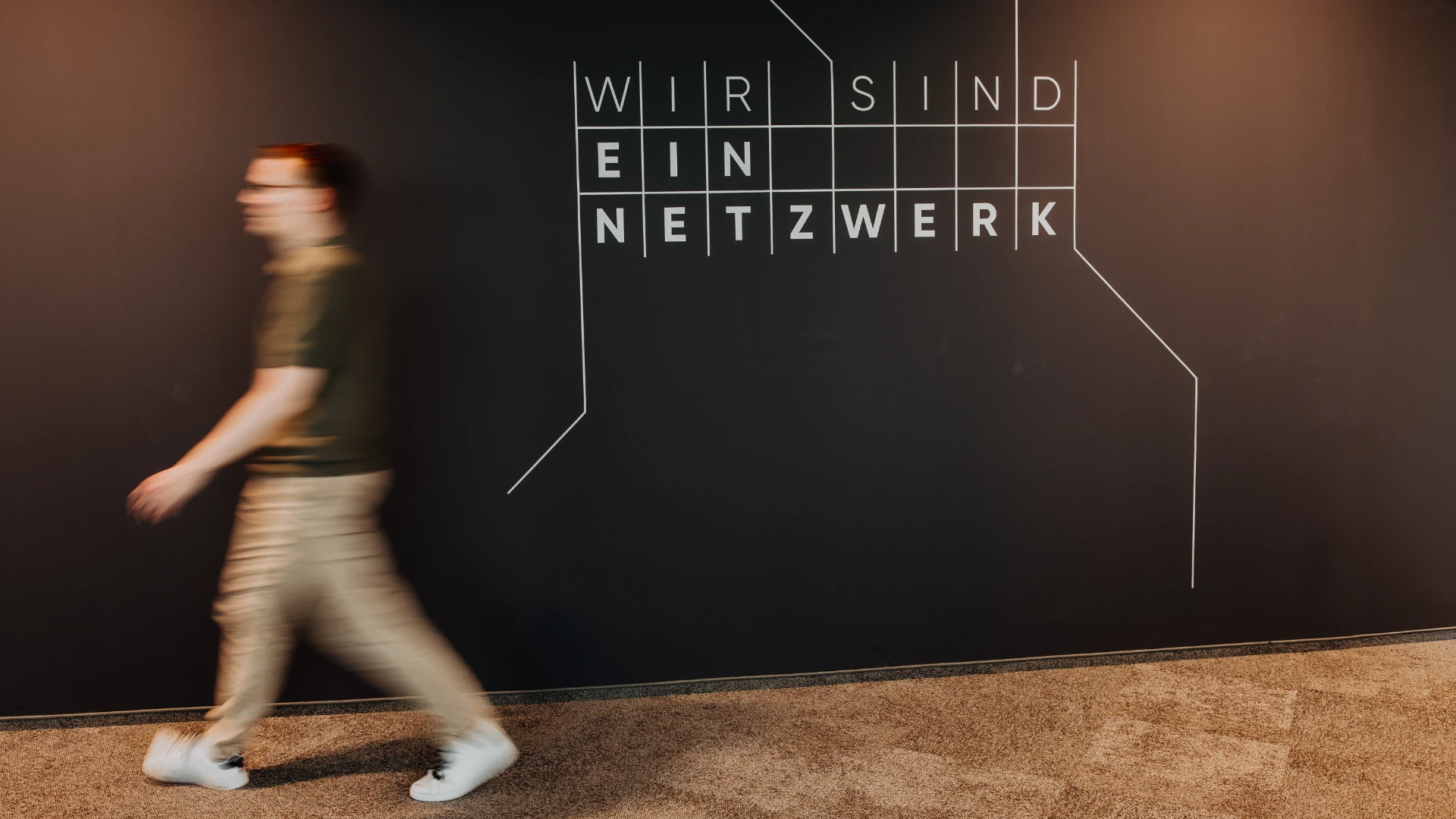 An employee walks past a wall reading “We are a network” — modern office design and a strong sense of connection reflect the open culture and attractive work environment at BSI Software.