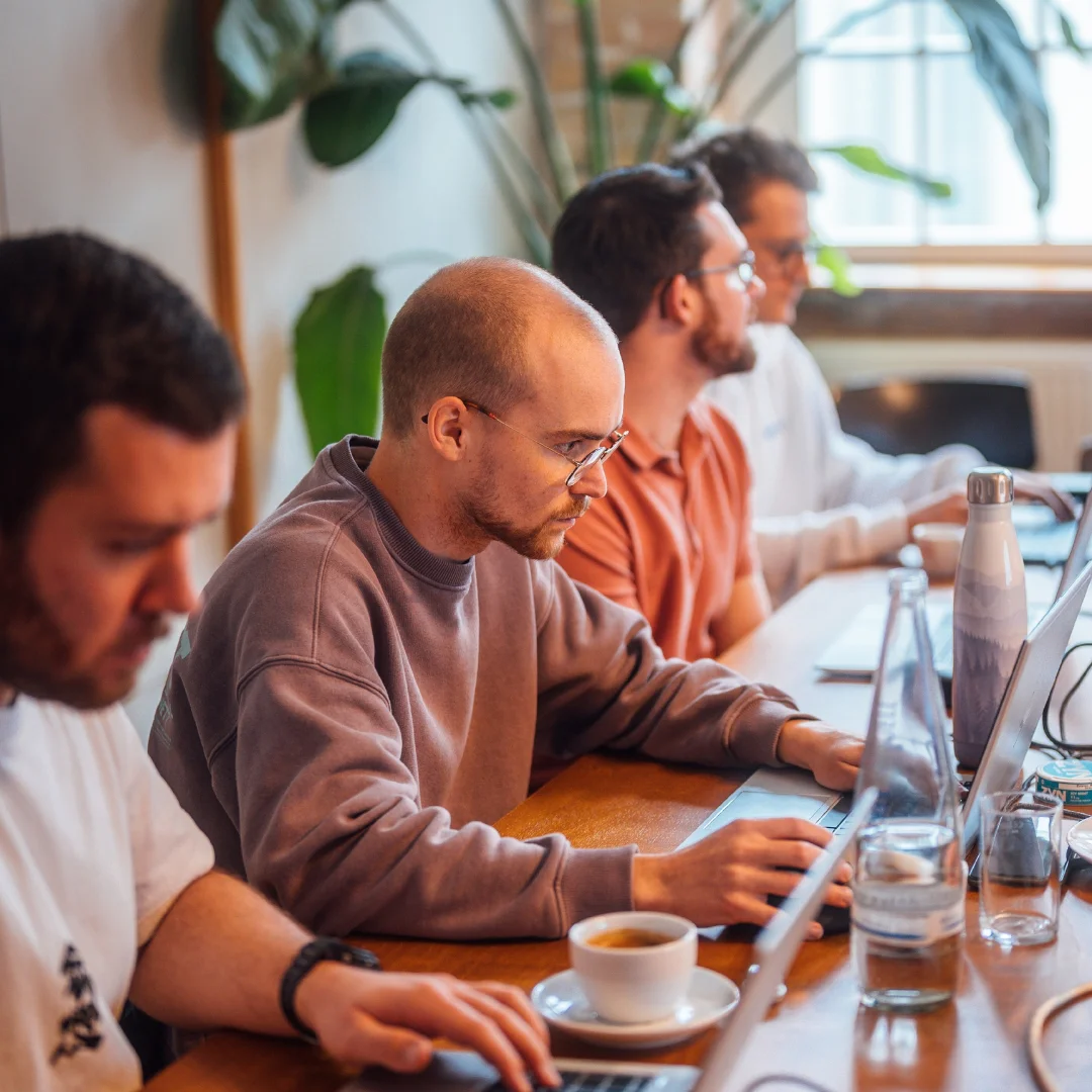 Participants work attentively on laptops during a workshop or training session in a modern workspace. Coffee, water bottles, and collaborative exchange create a productive learning atmosphere. The scene represents hands-on professional development and collaborative learning with the BSI Academy.