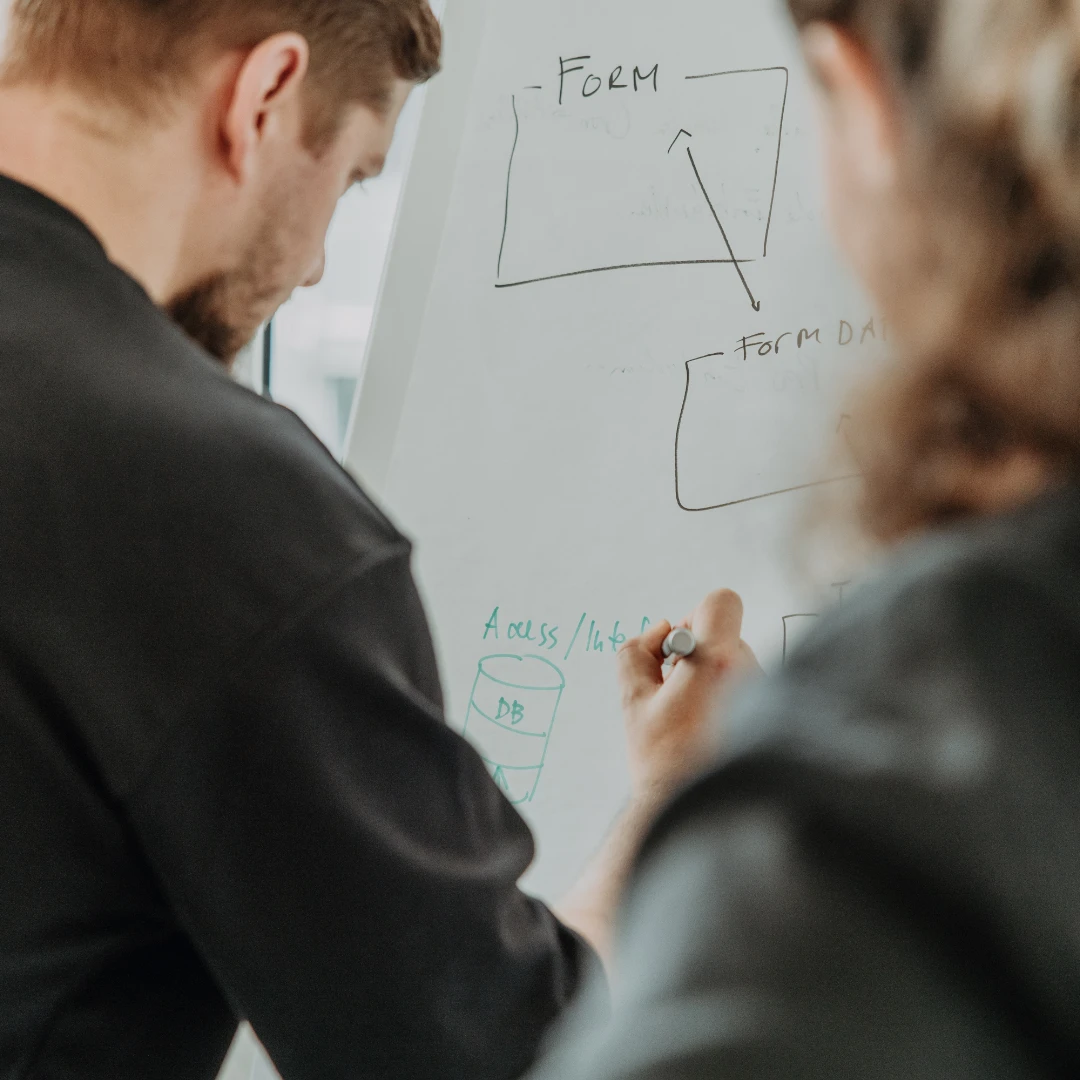 Zwei Personen skizzieren an einem Whiteboard einen digitalen Form-Workflow mit Pfeilen, «Form» und Datenfluss zur Datenbank.