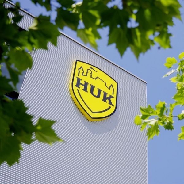 HUK-COBURG logo on a modern building facade, framed by green treetops against a blue sky.