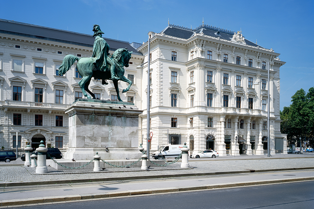 Historic equestrian statue in front of an ornate 19th-century building in Vienna under a blue sky.