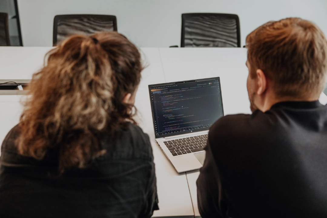 Two employees collaborate on a laptop, analyzing code—hands-on training, close mentoring, and insights into software development during an apprenticeship at BSI Software in Switzerland.