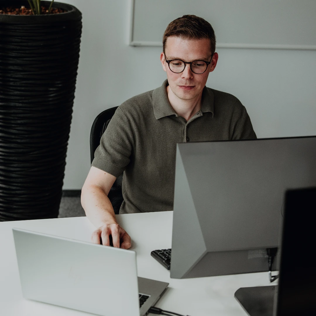 An experienced employee works focused at a laptop and monitor in a modern office—independent work, professional expertise, and strong development opportunities for experienced professionals at BSI Software.