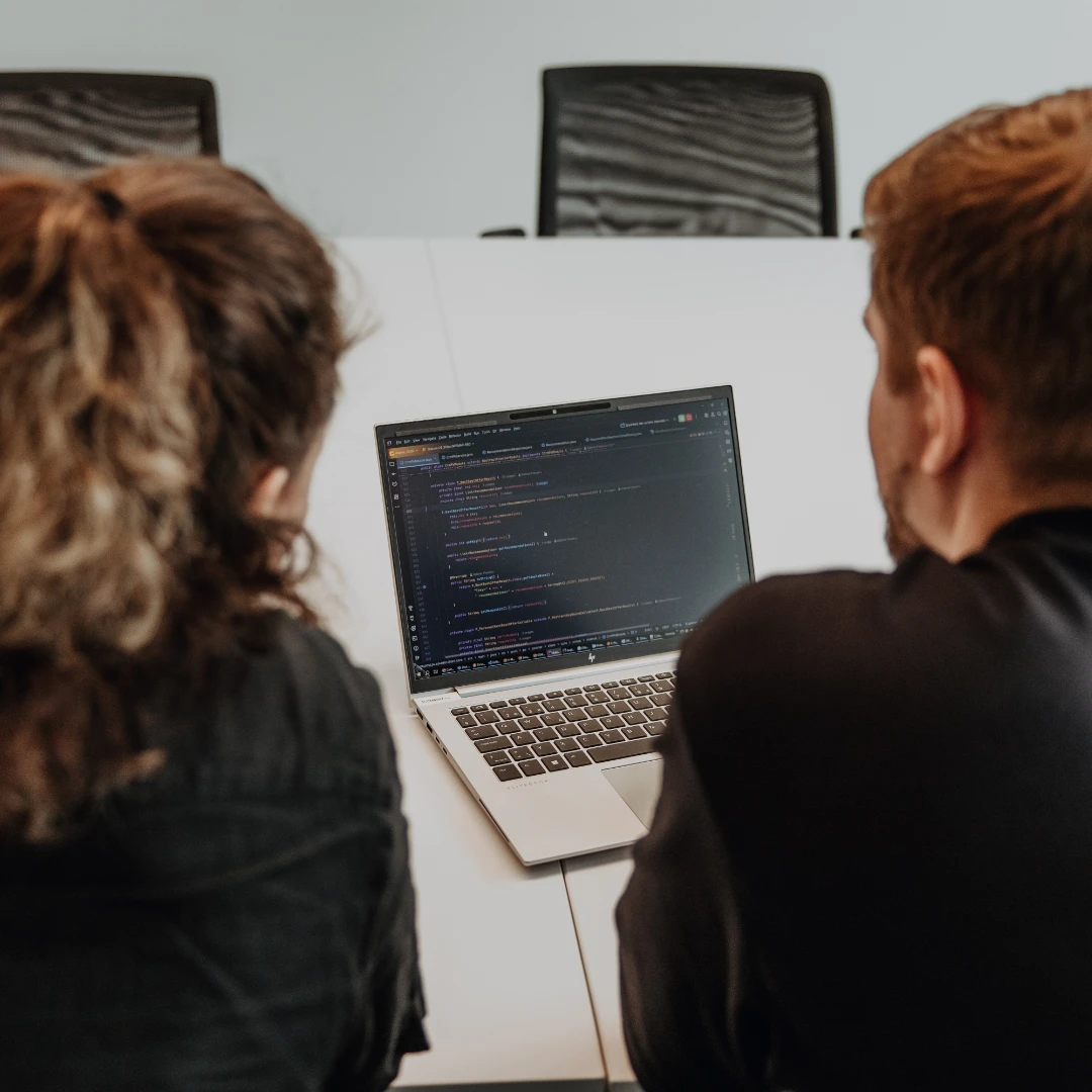 Zwei Mitarbeitende arbeiten gemeinsam am Laptop und analysieren Code – praxisnahe Ausbildung, enge Begleitung und Einblicke in die Softwareentwicklung während der Lehre bei BSI Software in der Schweiz.