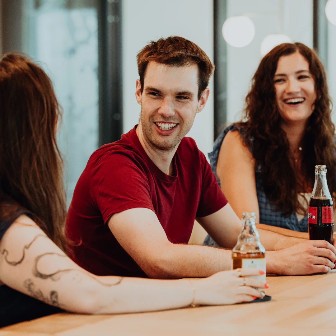 Three employees sit together, laughing and chatting over drinks—an open, friendly atmosphere and strong team culture at BSI Software that makes everyday work engaging and human.